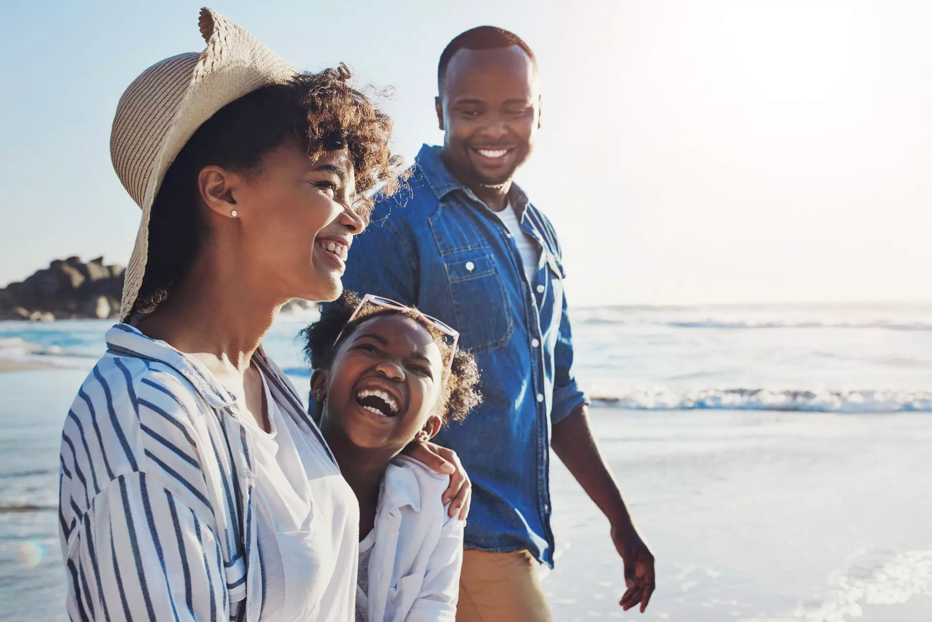 A family of three walking along the beach on vacation.