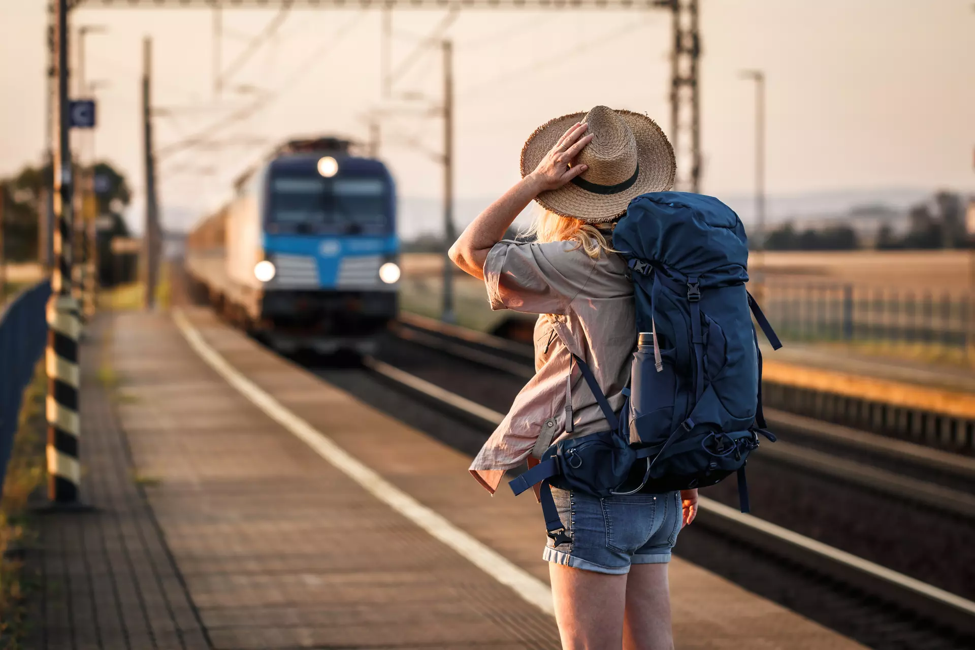 A girl in a hat waiting for a train at a train station.